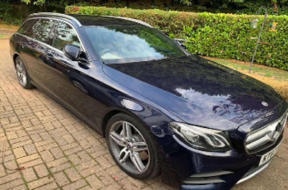 A dark blue Mercedes Estate Car, parked on a brick driveway with greenery in the background.